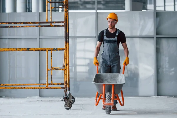 El arabalarıyla yürüyor. Gri üniformalı adam gündüz vakti modern büyük ofiste çalışıyor..