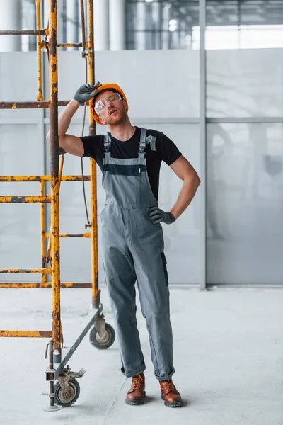 Gri üniformalı bir adam inşaatın yanında duruyor. Gündüz vakti modern büyük ofiste..