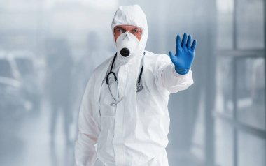 El hareketlerini durdurur. Laboratuvar önlüklü, koruyucu gözlüklü ve maskeli bir erkek doktor..