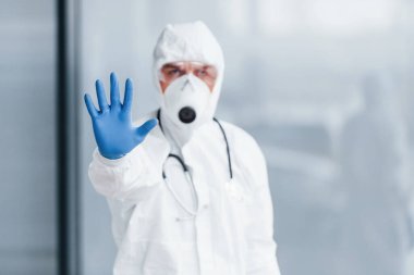 El hareketlerini durdurur. Laboratuvar önlüklü, koruyucu gözlüklü ve maskeli bir erkek doktor..