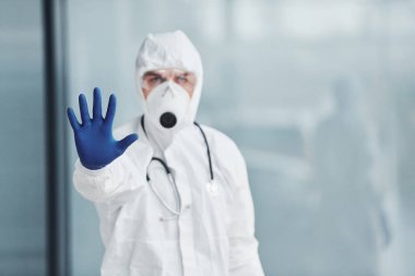 El hareketlerini durdurur. Laboratuvar önlüklü, koruyucu gözlüklü ve maskeli bir erkek doktor..
