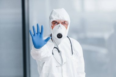 El hareketlerini durdurur. Laboratuvar önlüklü, koruyucu gözlüklü ve maskeli bir erkek doktor..
