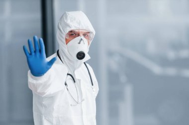 El hareketlerini durdurur. Laboratuvar önlüklü, koruyucu gözlüklü ve maskeli bir erkek doktor..