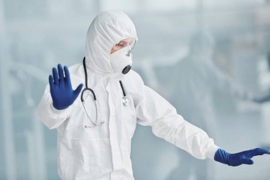 El hareketlerini durdurur. Laboratuvar önlüklü, koruyucu gözlüklü ve maskeli bir erkek doktor..