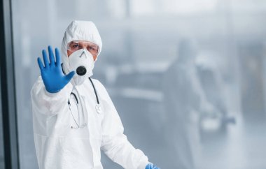 El hareketlerini durdurur. Laboratuvar önlüklü, koruyucu gözlüklü ve maskeli bir erkek doktor..