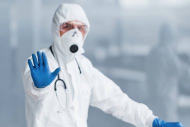 El hareketlerini durdurur. Laboratuvar önlüklü, koruyucu gözlüklü ve maskeli bir erkek doktor..