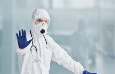 El hareketlerini durdurur. Laboratuvar önlüklü, koruyucu gözlüklü ve maskeli bir erkek doktor..