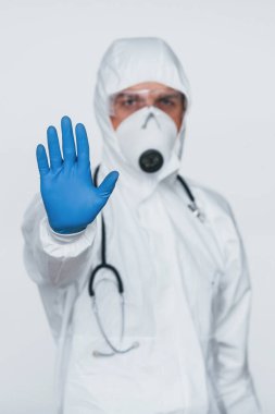 Shows stop gesture by hand. Male doctor scientist in lab coat, defensive eyewear and mask.
