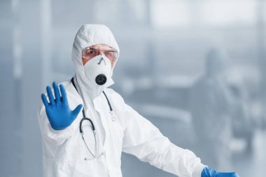 El hareketlerini durdurur. Laboratuvar önlüklü, koruyucu gözlüklü ve maskeli bir erkek doktor..