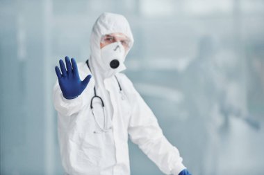 El hareketlerini durdurur. Laboratuvar önlüklü, koruyucu gözlüklü ve maskeli bir erkek doktor..