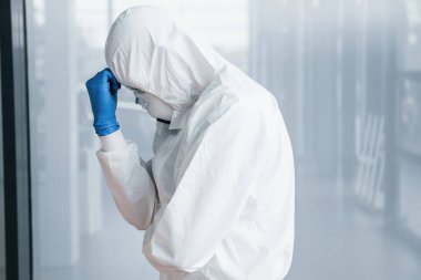Laboratuvar önlüklü, koruyucu gözlüklü ve maskeli erkek doktor kötü, bitkin ve hasta hissediyor..