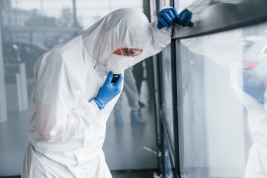 Laboratuvar önlüklü, koruyucu gözlüklü ve maskeli erkek doktor kötü, bitkin ve hasta hissediyor..