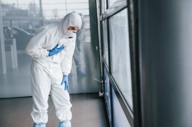 Laboratuvar önlüklü, koruyucu gözlüklü ve maskeli erkek doktor kötü, bitkin ve hasta hissediyor..