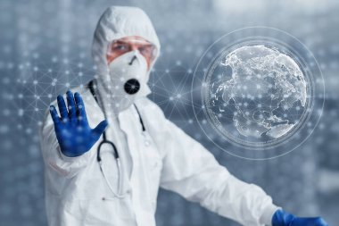 Digital world map on picture. Male doctor scientist in lab coat, defensive eyewear and mask standing indoors.