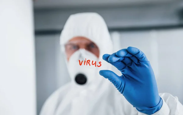 身穿实验室外套 戴防卫性眼镜 戴口罩的男医生拿着装有病毒字样的玻璃杯 — 图库照片