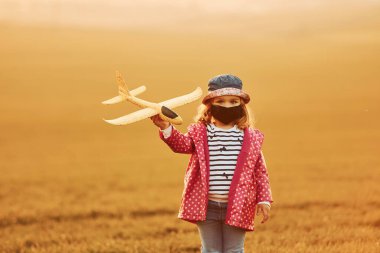 Turuncu renkli güneş ışığıyla aydınlatılmış. Sevimli küçük kız oyuncak uçakla gündüz vakti güzel tarlada eğlen..