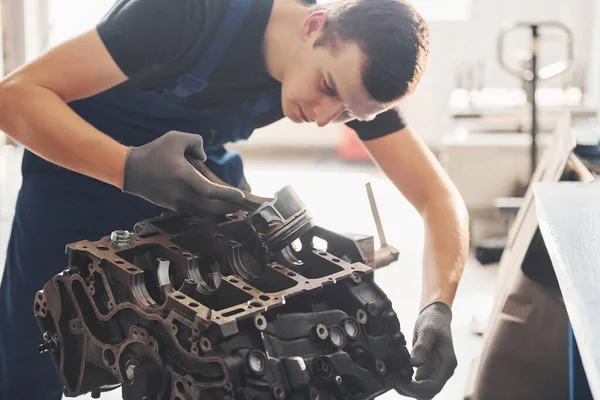 Professional repairman works with broken automobile engine.