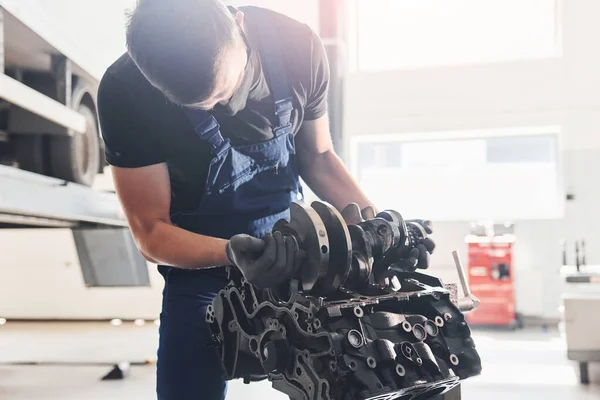 Professional repairman works with broken automobile engine.