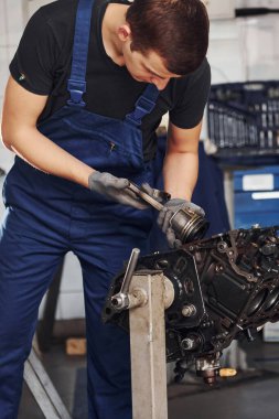 Professional repairman in garage works with broken automobile engine.
