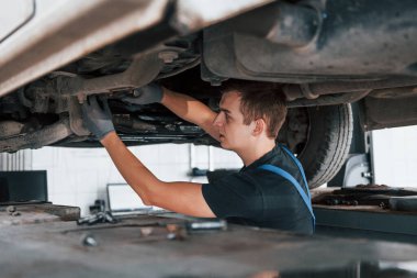 Siyah gömlekli profesyonel tamirci bozuk bir otomobilin altında çalışır..