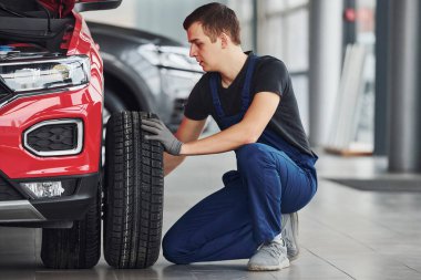Üniformalı bir adam otomobilin lastiğini değiştiriyor. Araba hizmeti kavramı.