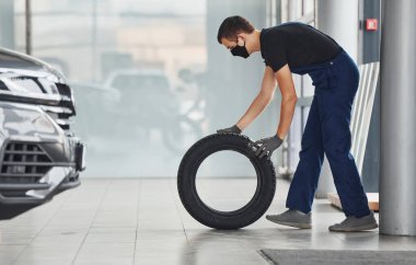 Siyah-mavi üniformalı bir işçi araba direksiyonu tutuyor ve içeride çalışıyor..