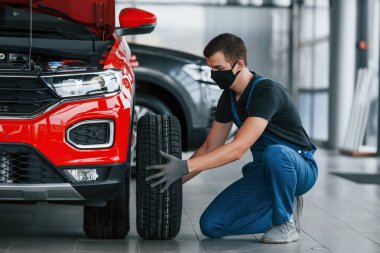 Üniformalı bir adam otomobilin lastiğini değiştiriyor. Araba hizmeti kavramı.