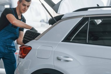 Siyah-mavi üniformalı işçiler araba tekerleğini beyaz otomobilin içine yerleştirdiler..