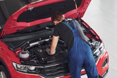 Kırmızı otomobili tamir eden üniformalı erkek işçinin üst görüntüsü.