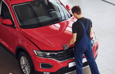 Top view of male worker in uniform that repairs red automobile.