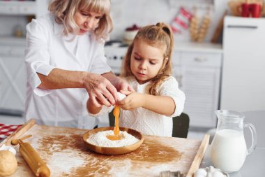 Yumurta kullanıyor. Büyük büyükanne ve küçük torunu mutfakta Noel için tatlı pişiriyor..