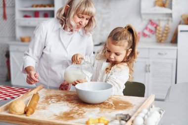 İçi süt dolu. Büyük büyükanne ve küçük torunu mutfakta Noel için tatlı pişiriyor..