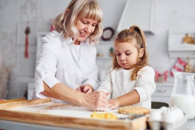 Öğretim süreci. Büyük büyükanne ve küçük torunu mutfakta Noel için tatlı pişiriyor..
