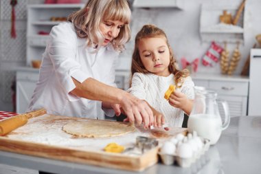 Öğretim süreci. Büyük büyükanne ve küçük torunu mutfakta Noel için tatlı pişiriyor..