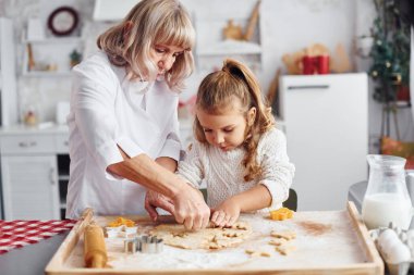 Öğretim süreci. Büyük büyükanne ve küçük torunu mutfakta Noel için tatlı pişiriyor..