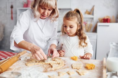 Öğretim süreci. Büyük büyükanne ve küçük torunu mutfakta Noel için tatlı pişiriyor..