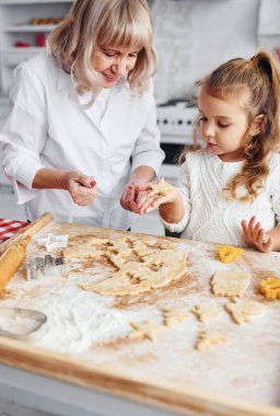 Öğretim süreci. Büyük büyükanne ve küçük torunu mutfakta Noel için tatlı pişiriyor..