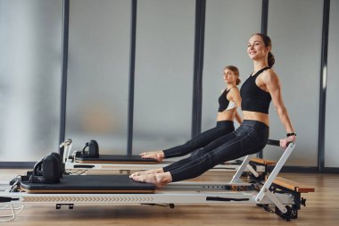 Eller güçlü. Spor elbiseli ve zayıf vücutlu iki kadın kapalı alanda spor yoga yapıyorlar..