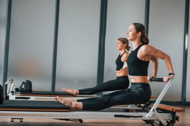 Eller güçlü. Spor elbiseli ve zayıf vücutlu iki kadın kapalı alanda spor yoga yapıyorlar..