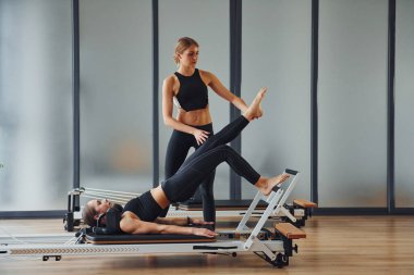 Trainer helping girl. Two women in sportive wear and with slim bodies have fitness yoga day indoors together.