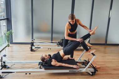 Learns new exercises. Two women in sportive wear and with slim bodies have fitness yoga day indoors together.
