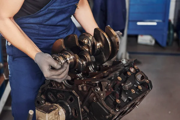 Professional repairman in garage works with broken automobile engine.