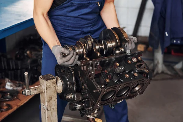 Professional repairman in garage works with broken automobile engine.