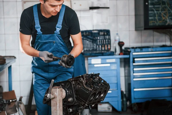 Professional repairman in garage works with broken automobile engine.