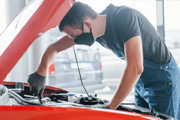 Man in uniform works with broken automobile. Conception of car service.