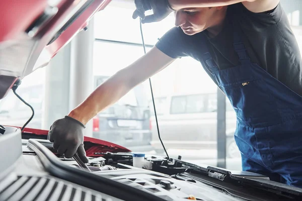 Man in uniform works with broken automobile. Conception of car service.