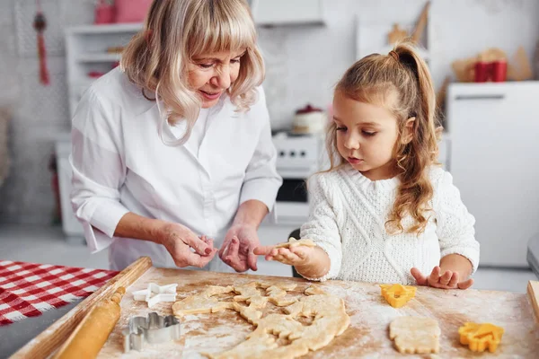 Öğretim süreci. Büyük büyükanne ve küçük torunu mutfakta Noel için tatlı pişiriyor..