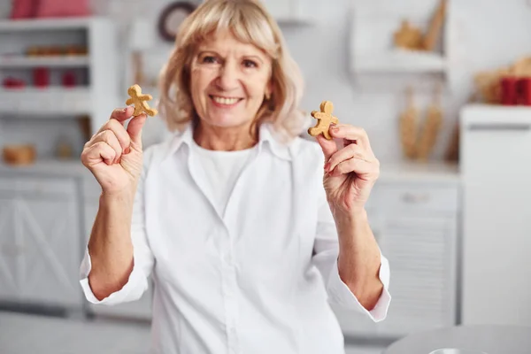 Senior woman cooks Christmas cookies on the kitchen at daytime.