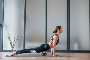 Yandan bak. Spor elbiseli ve zayıf vücutlu genç bir kadın kapalı alanda spor yoga yapıyor..