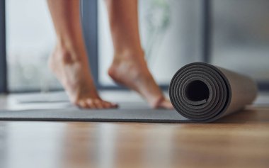 Mindere odaklanmış görüntüyü kapat. Spor elbiseli ve zayıf vücutlu genç bir kadın kapalı alanda spor yoga yapıyor..